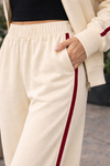 Close-up detail of women’s ivory wide leg athleisure track pants with crimson stripe, elastic waistband, and pocket styling in casual lifestyle outfit