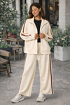 Latina woman wearing ivory and crimson stripe athleisure track jacket and wide leg lounge pants styled with black t-shirt and trendy sneakers in casual everyday outfit