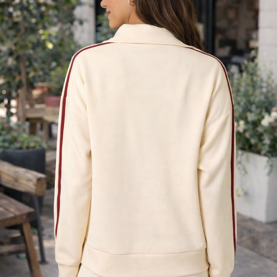 Back view of Latina woman wearing ivory and crimson stripe women's athleisure track jacket and matching lounge pants styled as casual everyday outfit