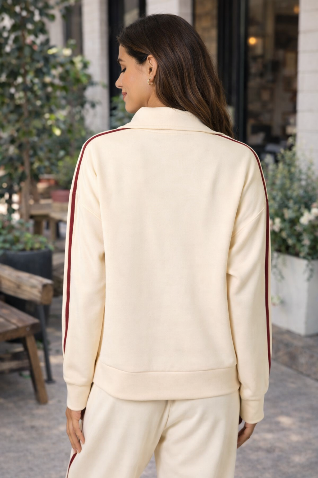 Back view of Latina woman wearing ivory and crimson stripe women's athleisure track jacket and matching lounge pants styled as casual everyday outfit