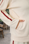 Close-up detail of women's ivory track jacket with crimson side stripe and front pocket showing soft athleisure fabric in lifestyle outfit