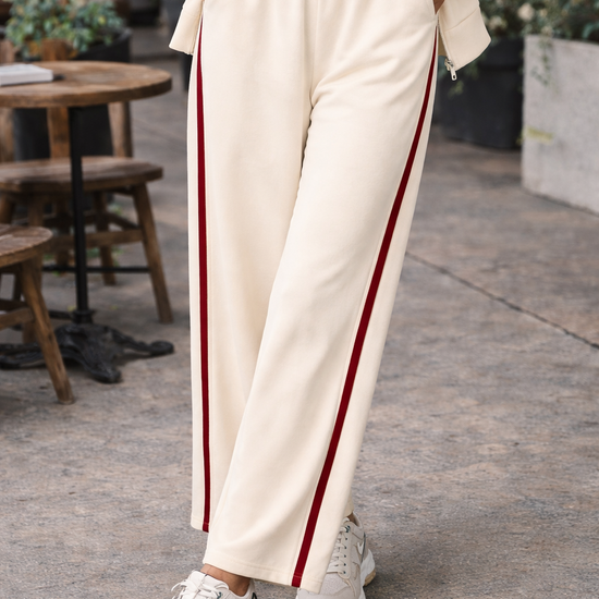 Women's ivory wide leg athleisure pants with crimson side stripe styled with sneakers in casual everyday outfit at outdoor café