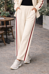 Women's ivory wide leg athleisure pants with crimson side stripe styled with sneakers in casual everyday outfit at outdoor café