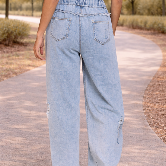 Back view of light wash distressed wide leg jeans with paper bag waist and drawstring detail in a relaxed outdoor setting