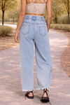 Back view of light wash distressed wide leg jeans with paper bag waist and drawstring detail in a relaxed outdoor setting