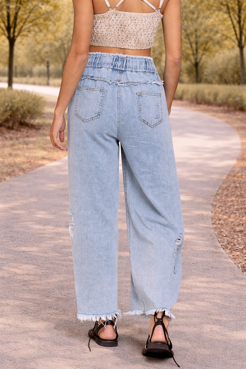 Back view of light wash distressed wide leg jeans with paper bag waist and drawstring detail in a relaxed outdoor setting