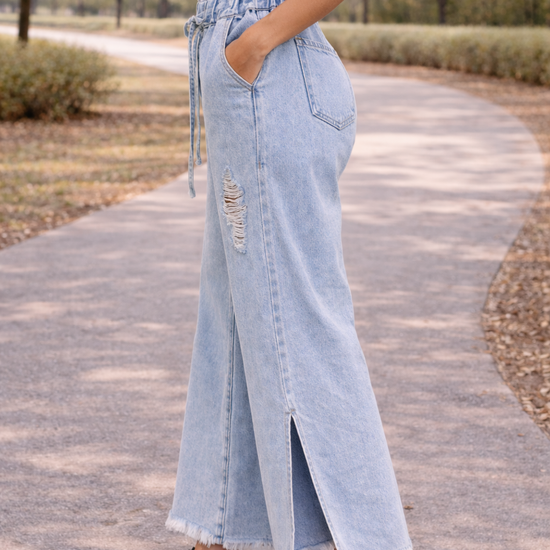 Side view of light wash distressed wide leg jeans with paper bag waist and drawstring detail, styled in a casual outdoor setting