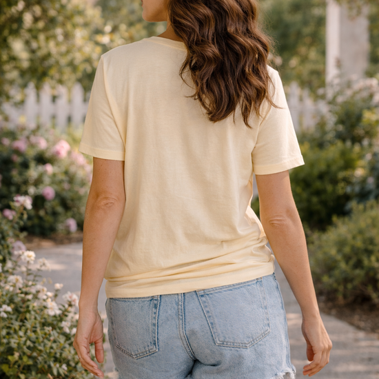 back view of woman wearing mama goose graphic tee with denim shorts walking on a sunlit garden path