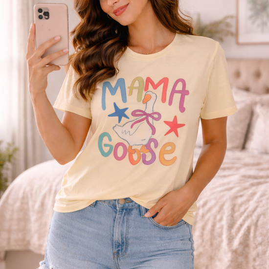 woman wearing mama goose graphic tee taking mirror selfie in a cozy bedroom wearing denim shorts