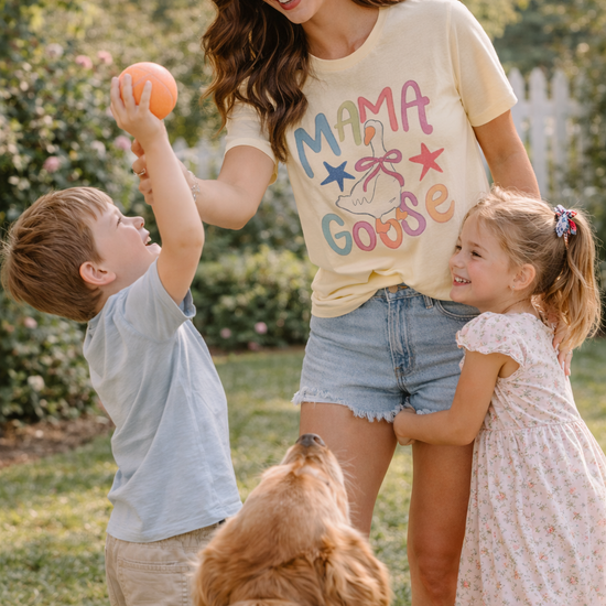 mom wearing mama goose graphic tee playing outside with two children and a dog in a sunny backyard setting