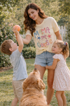 mom wearing mama goose graphic tee playing outside with two children and a dog in a sunny backyard setting