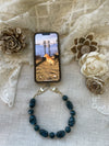 Midnight teal phone wristlet attached to a phone on a neutral textured background