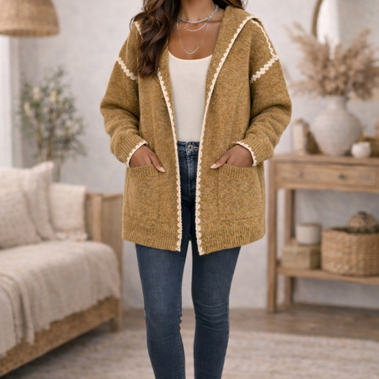 Woman wearing a mustard hooded boho cardigan with trim, jeans, ankle boots and a white tank top in a cozy living room.