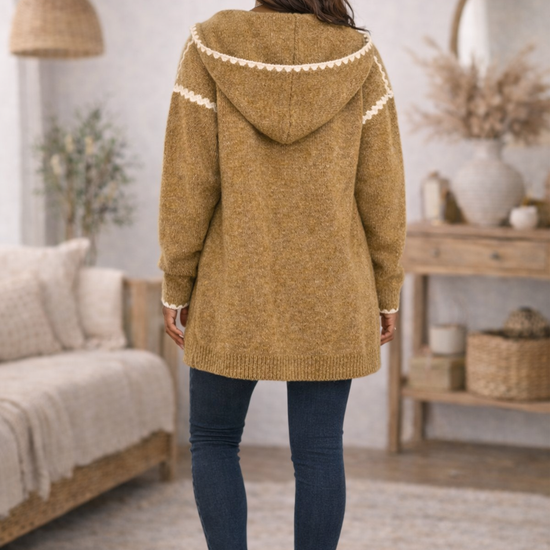 The backside of a mustard hooded boho cardigan and jeans in a cozy living room

