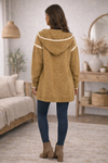 The backside of a mustard hooded boho cardigan and jeans in a cozy living room
