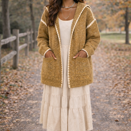 Woman wearing a cream dress and a mustard hooded boho cardigan outside in a fall setting