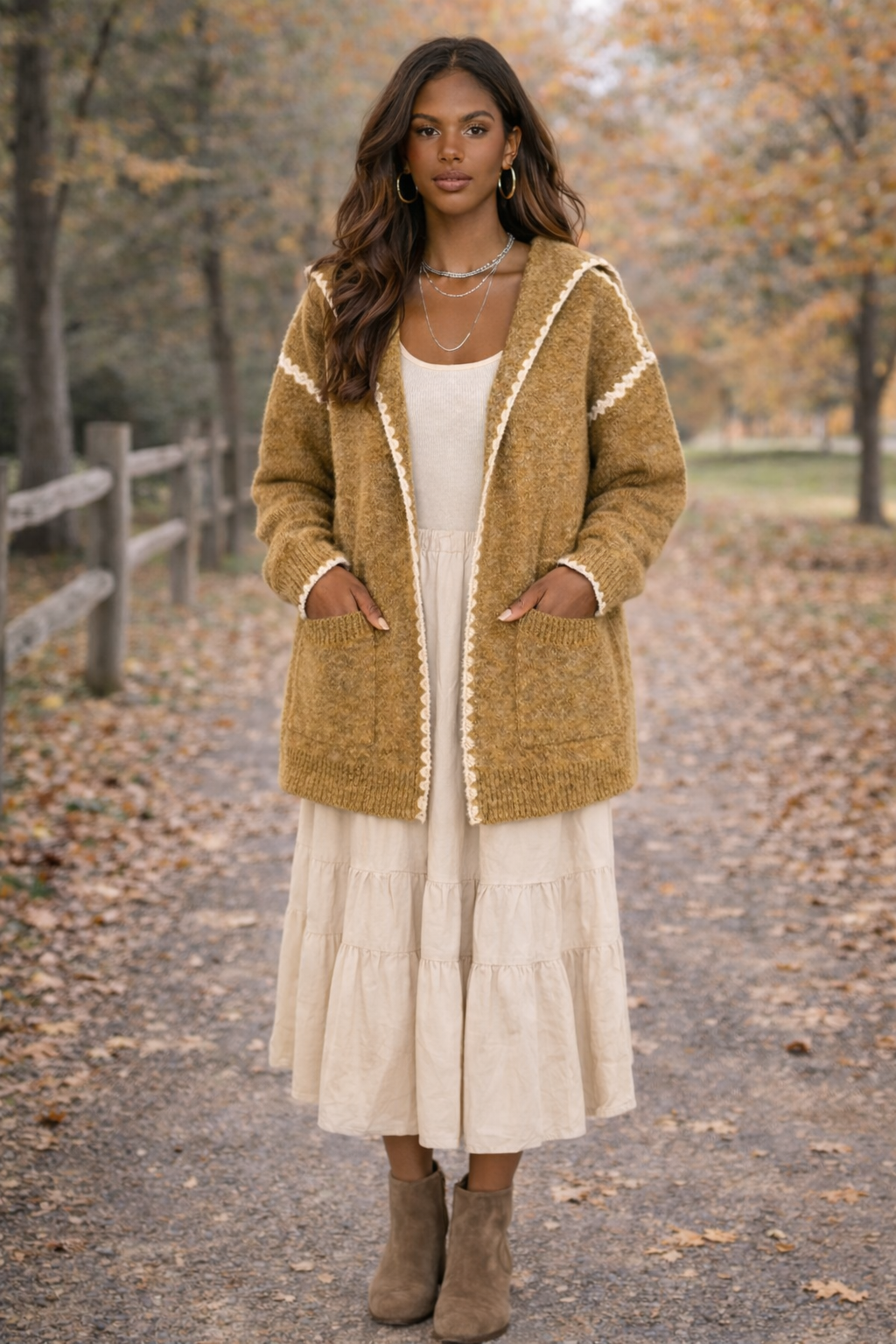 Woman wearing a cream dress and a mustard hooded boho cardigan outside in a fall setting