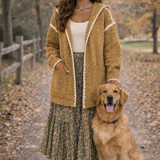 Woman wearing a white top, flowery skirt and a mustard hooded boho cardigan, in an outside fall setting with a golden retriever