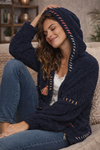 Navy boho textured cozy zip jacket with artisan stitching and hood shown from back on brunette model in a warm neutral living room interior.