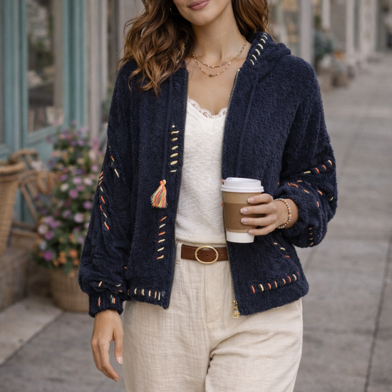 Brunette model wearing navy boho textured cozy zip jacket with artisan stitching styled with cream wide-leg pants holding coffee outside boutique storefront.