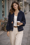 Brunette model wearing navy boho textured cozy zip jacket with artisan stitching styled with cream wide-leg pants holding coffee outside boutique storefront.