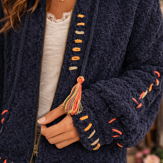 Close up of navy boho textured cozy zip jacket showing soft sherpa texture, colorful stitching and tassel detail.