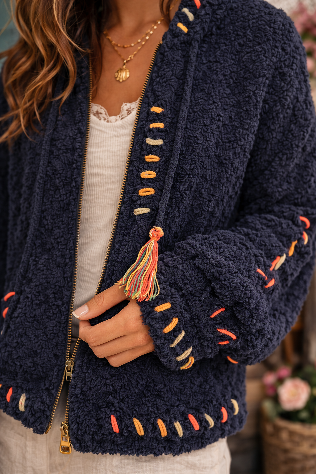Close up of navy boho textured cozy zip jacket showing soft sherpa texture, colorful stitching and tassel detail.
