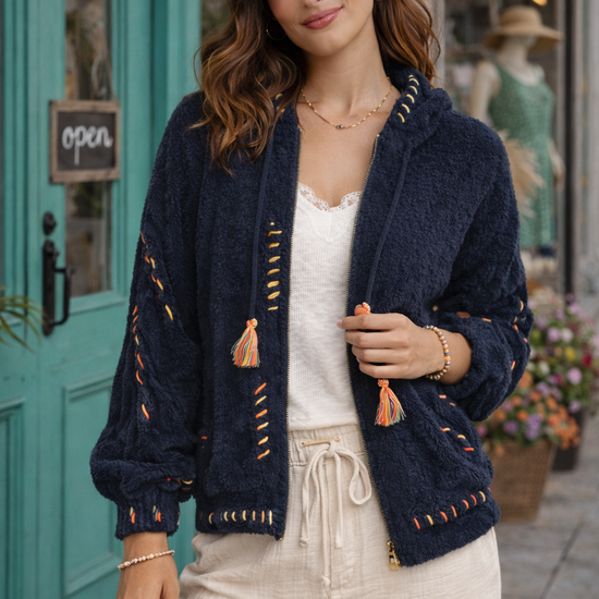 Navy boho textured cozy zip jacket with colorful stitching styled on brunette model wearing cream pants outside a boutique storefront.