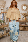 Woman wearing an off shoulder peasant top with sky blue boho patchwork wide leg pants in a store setting.
