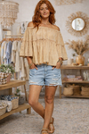 Woman wearing an off shoulder peasant boho top with distressed denim shorts in a boutique setting.