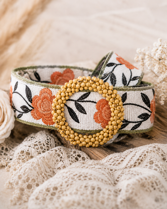 Close-up of the POL Boho Floral Statement Belt featuring orange floral embroidery, black leaf detailing, and a round wooden beaded buckle on a soft neutral boho background.