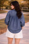 back view of woman wearing relaxed chambray button down top worn untucked with high waisted tailored shorts outdoors