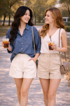 woman wearing relaxed chambray button down top with high waisted tailored shorts walking outdoors with friend holding iced coffee