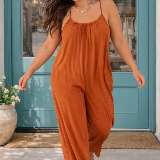 Woman walking in a rust wide-leg jumpsuit in front of a boutique with turquoise doors, styled as a comfortable casual everyday outfit