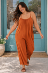 Woman walking in a rust wide-leg jumpsuit in front of a boutique with turquoise doors, styled as a comfortable casual everyday outfit