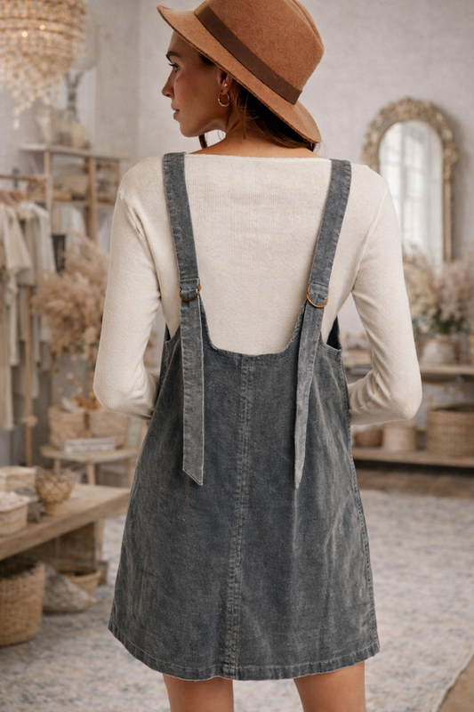 Woman wearing a sage corduroy pinafore dress and a wide brim hat in a boutique