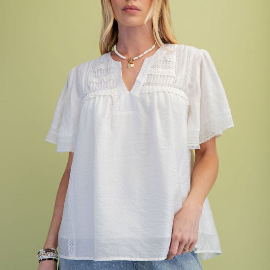 A model is wearing the Ivory Lace Pintuck Flutter Sleeve Blouse with a green background