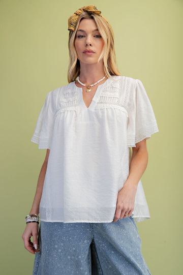 A model is wearing the Ivory Lace Pintuck Flutter Sleeve Blouse with a green background