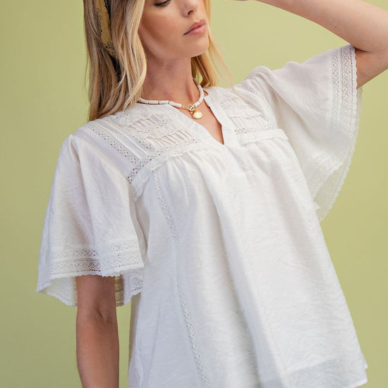 side view of a model wearing the Ivory Lace Pintuck Flutter Sleeve Blouse with a green background