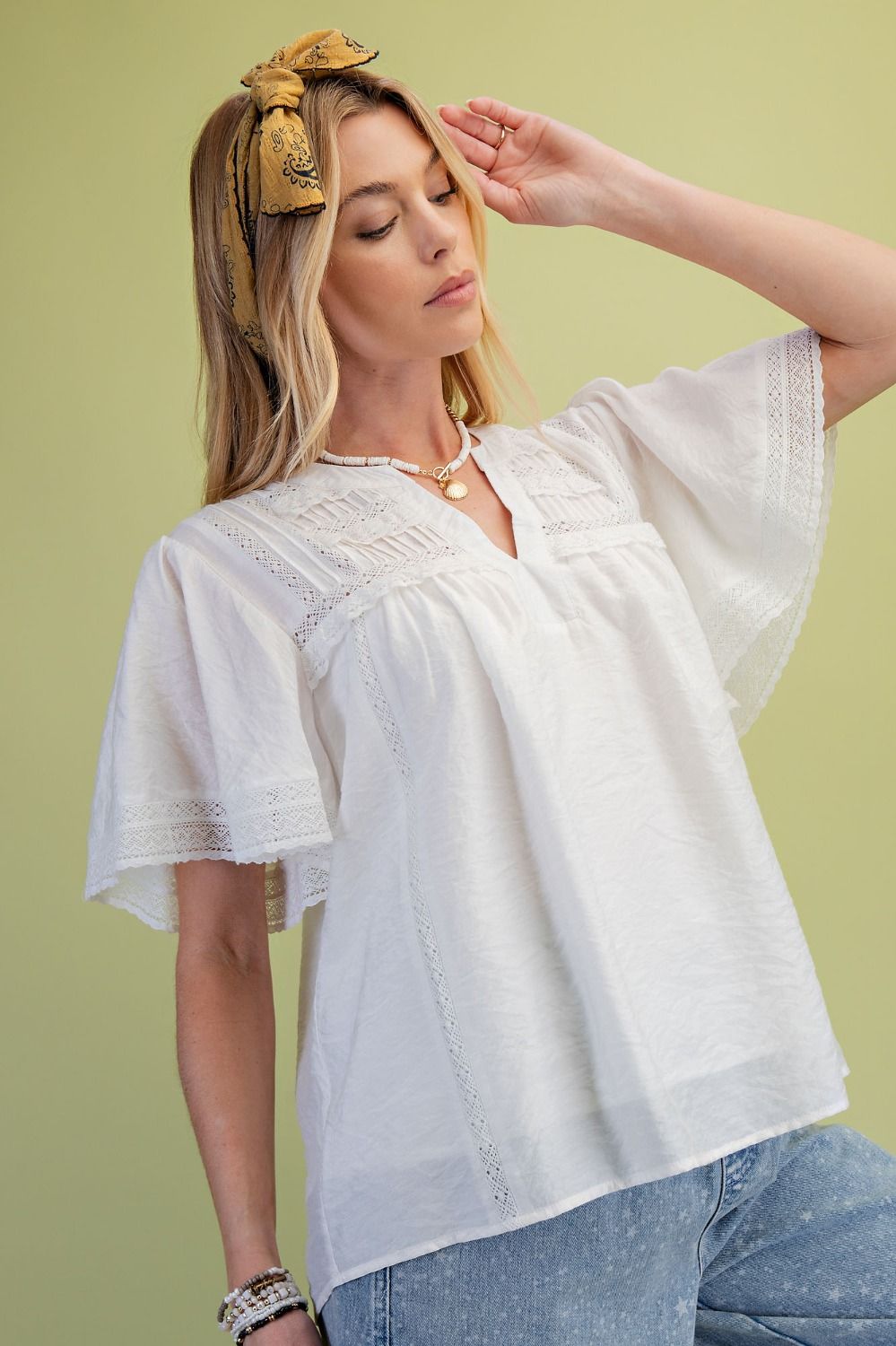 side view of a model wearing the Ivory Lace Pintuck Flutter Sleeve Blouse with a green background