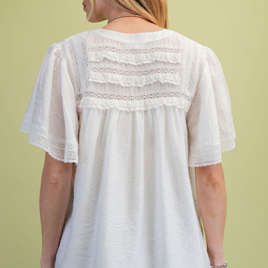 A model is standing in front of a green background showing the back view of the Ivory Lace Pintuck Flutter Sleeve Blouse