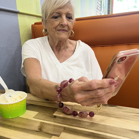 Woman wearing the shimmery berry orchid phone wristlet sitting at a table in an ice-cream shop