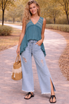 Woman wearing a teal flowy boho top with light wash distressed wide leg jeans styled in a casual outdoor outfit