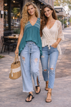 Two women walking in casual boho outfits featuring a teal flowy top and light wash distressed wide leg jeans styled for everyday wear