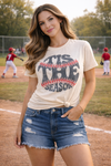 woman wearing tis the season baseball graphic tee with distressed denim shorts at baseball field