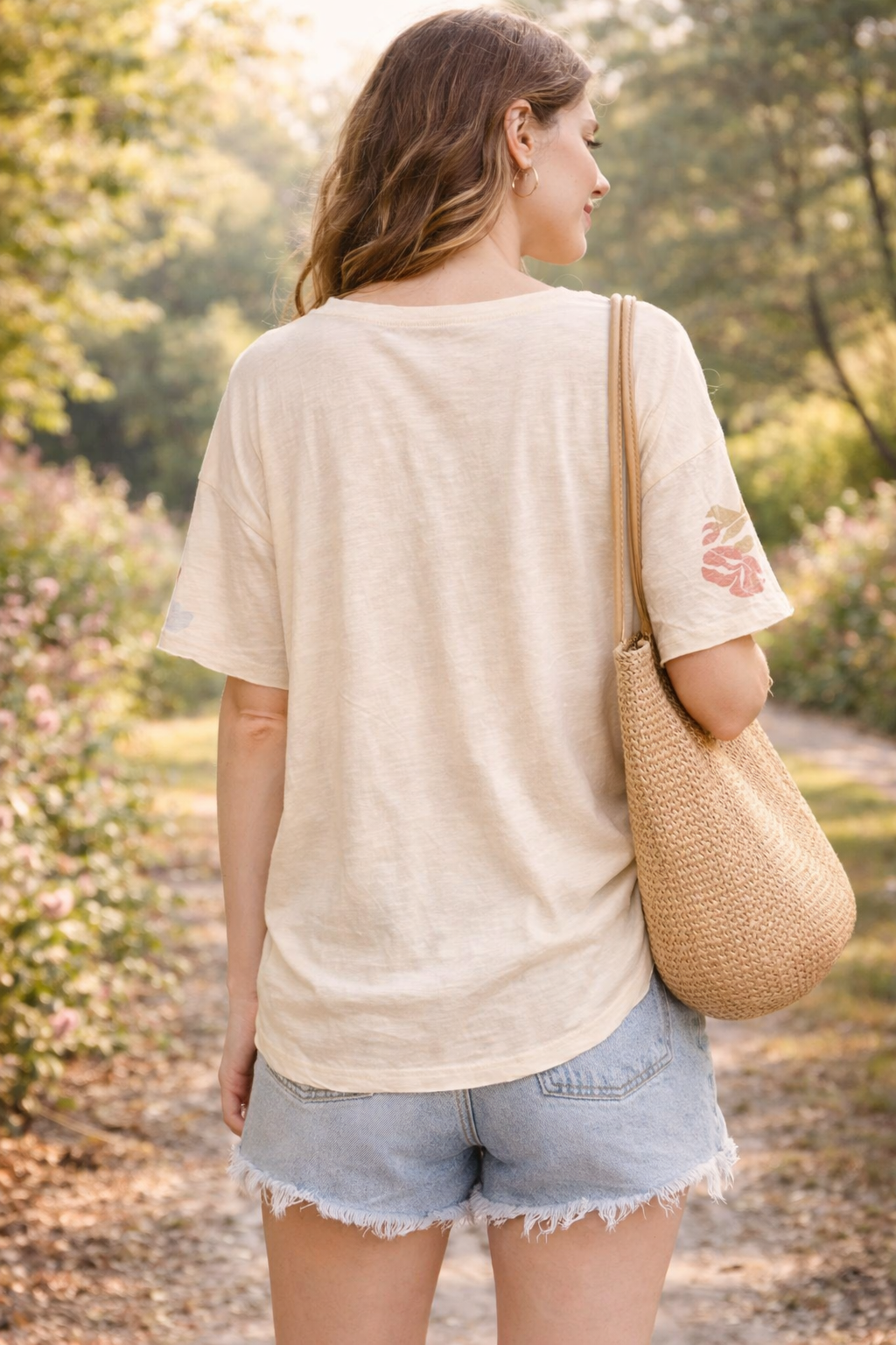 Back view of women's boho butterfly floral graphic tee styled with denim shorts in a relaxed boutique summer outfit