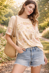 Women's boho butterfly floral graphic tee styled with denim shorts in a soft neutral botanical print boutique top