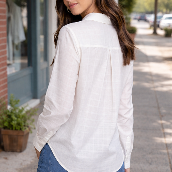 Back view of a woman wearing a lightweight white button-up blouse styled in a casual outdoor street setting