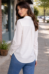 Back view of a woman wearing a lightweight white button-up blouse styled in a casual outdoor street setting