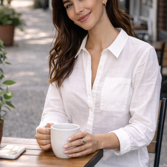 woman sitting at an outdoor café wearing a lightweight white button-up blouse styled with denim for a casual everyday outfit